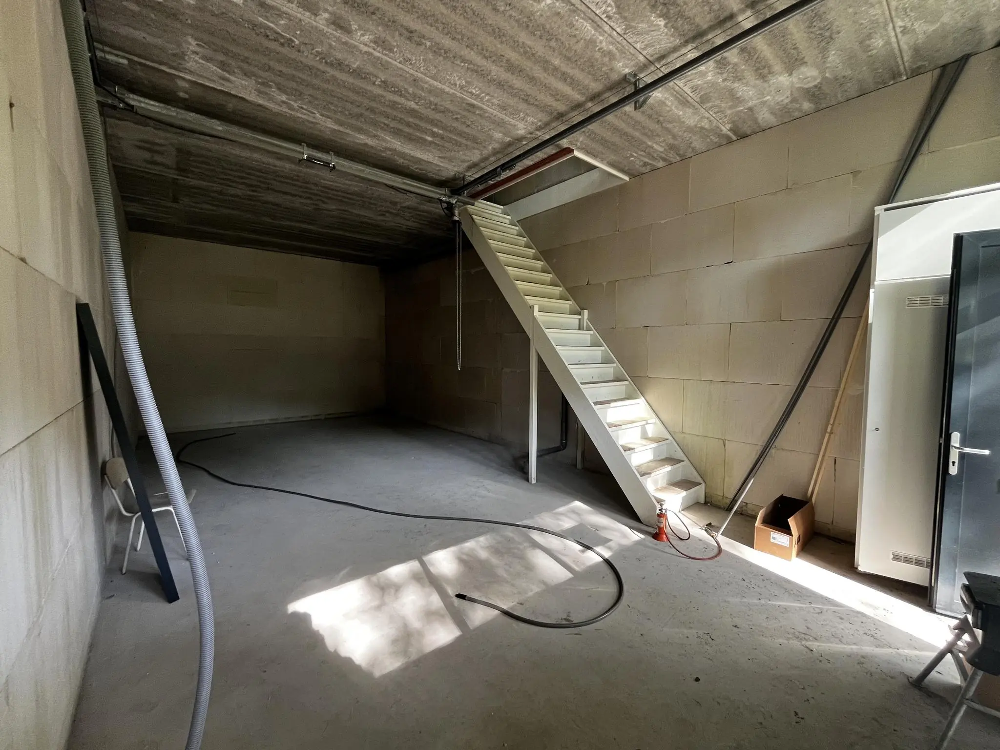 Lege bedrijfsruimte aan de Broekdijk West 19-10 met betonnen muren, trap naar boven en enkele losse voorwerpen op de vloer.